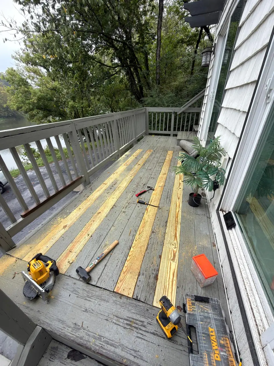 New wood boards installed among existing gray deck boards, with tools on site